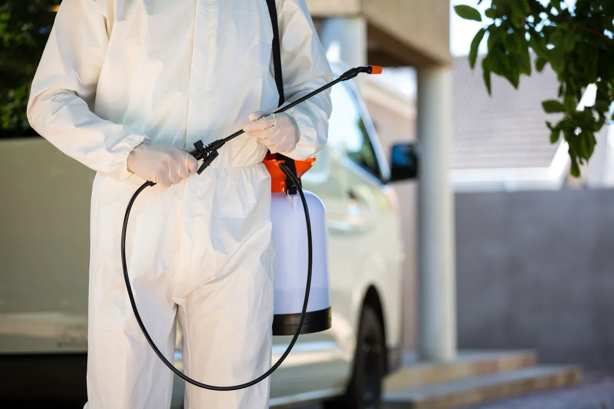 Pest control technician preparing a sprayer beside a service van at a home