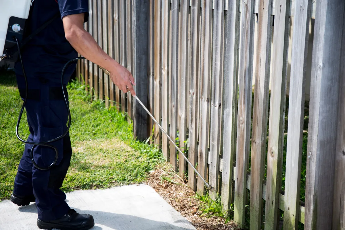 Technician treating the base of a wooden fence line in a Florida yard